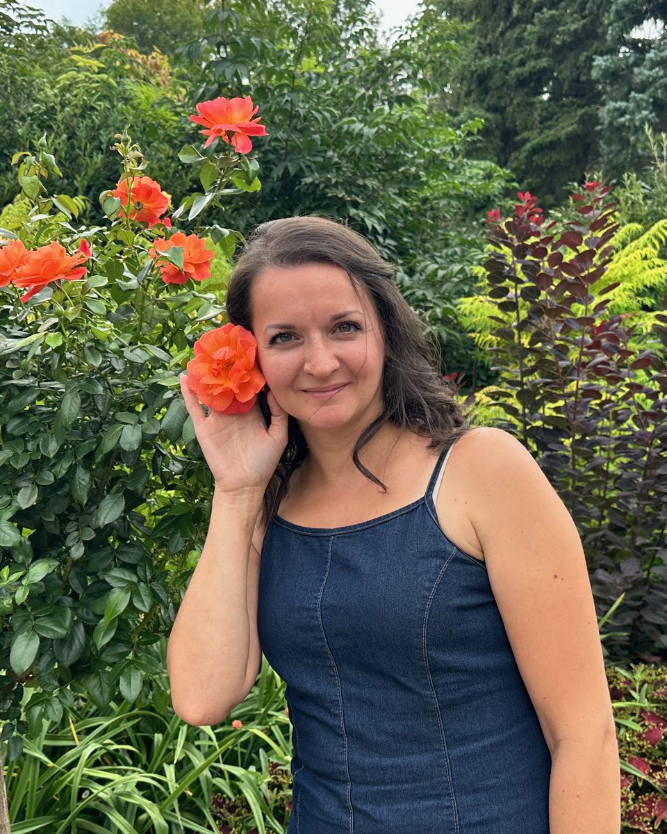 The mom behind Mom Money Hour, smiling in a garden with an orange rose